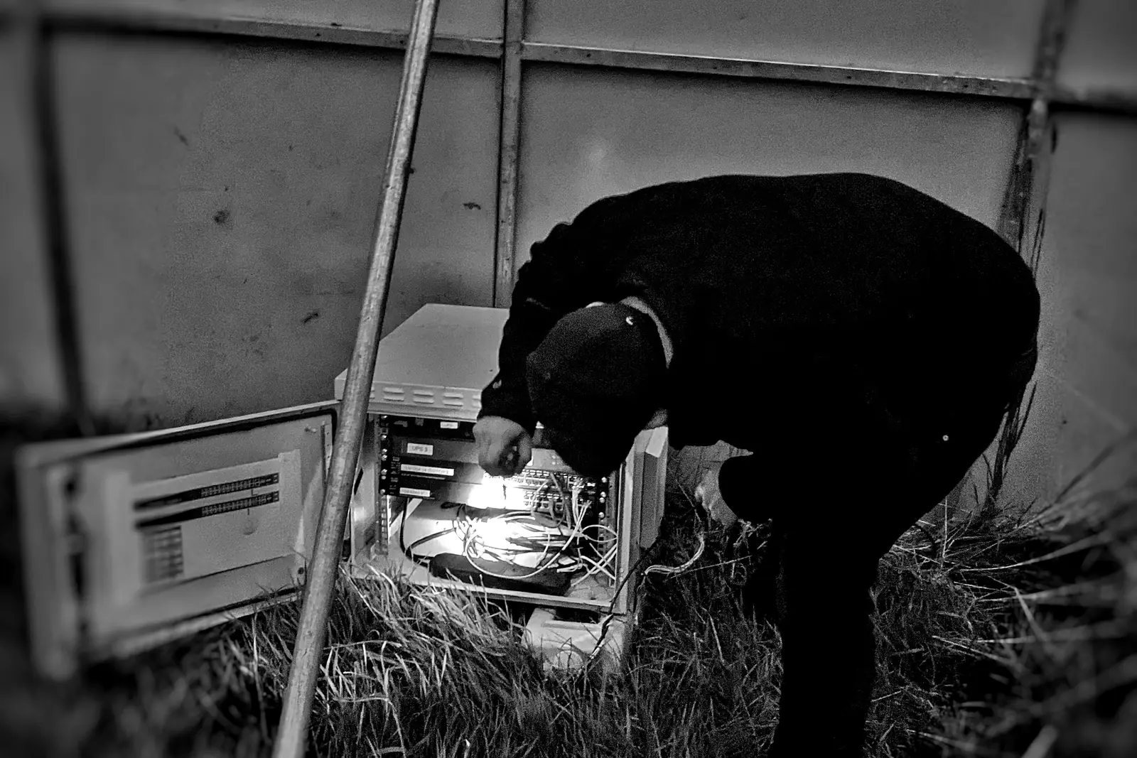 Black and white photo of a crew member bending over a kit box on the grass beside a tent leg.