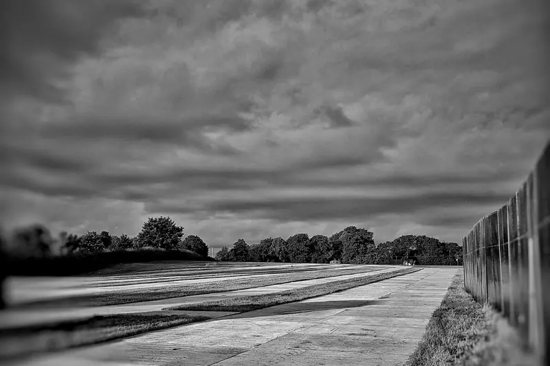 Black and white photo of a wide sky over an empty airfield road and fence.
