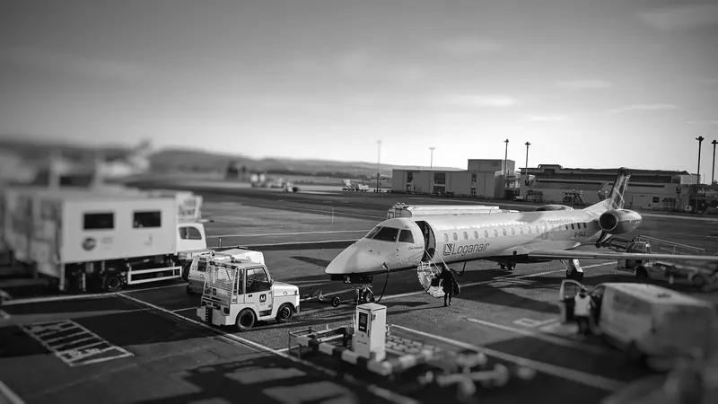 Black and white photo of a private jet and ground vehicles on an airport apron in the early morning.
