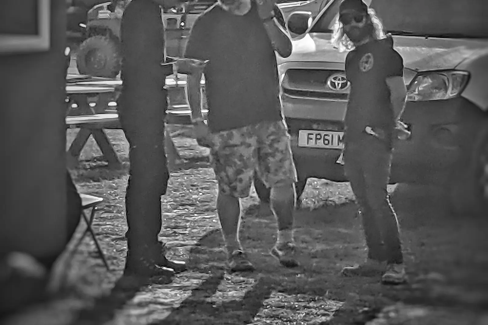 Black and white photo of crew talking beside vehicles on a festival site.