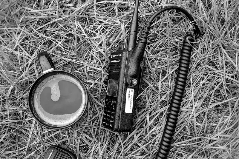 Black and white photo of a two way radio and earpiece lying on the grass.