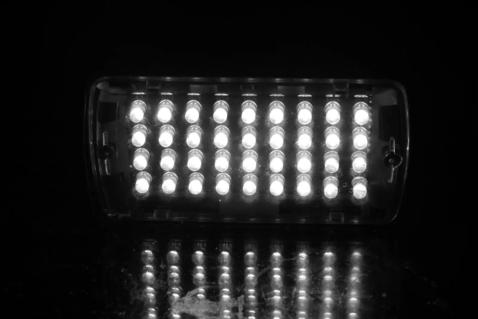 Black and white photo of a bank of stage lamps glowing in the dark, reflected on the stage below.