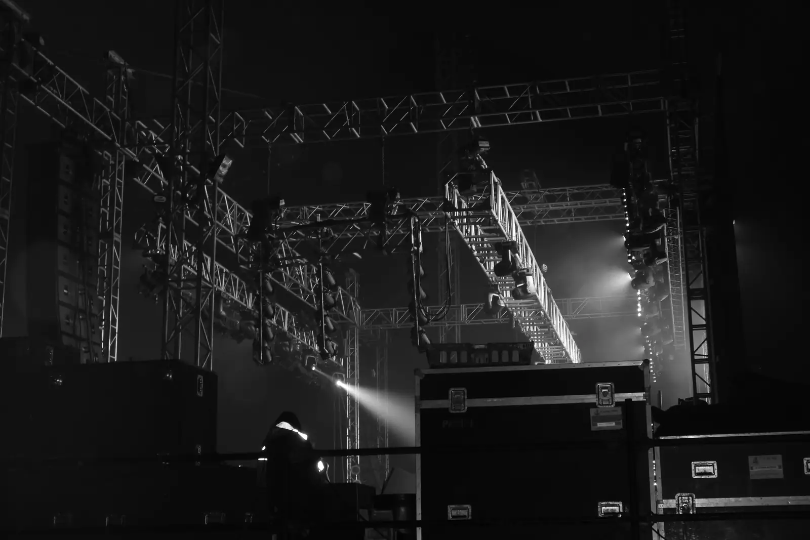 Black and white photo of a stage truss rig lit above flight cases on a dark stage.